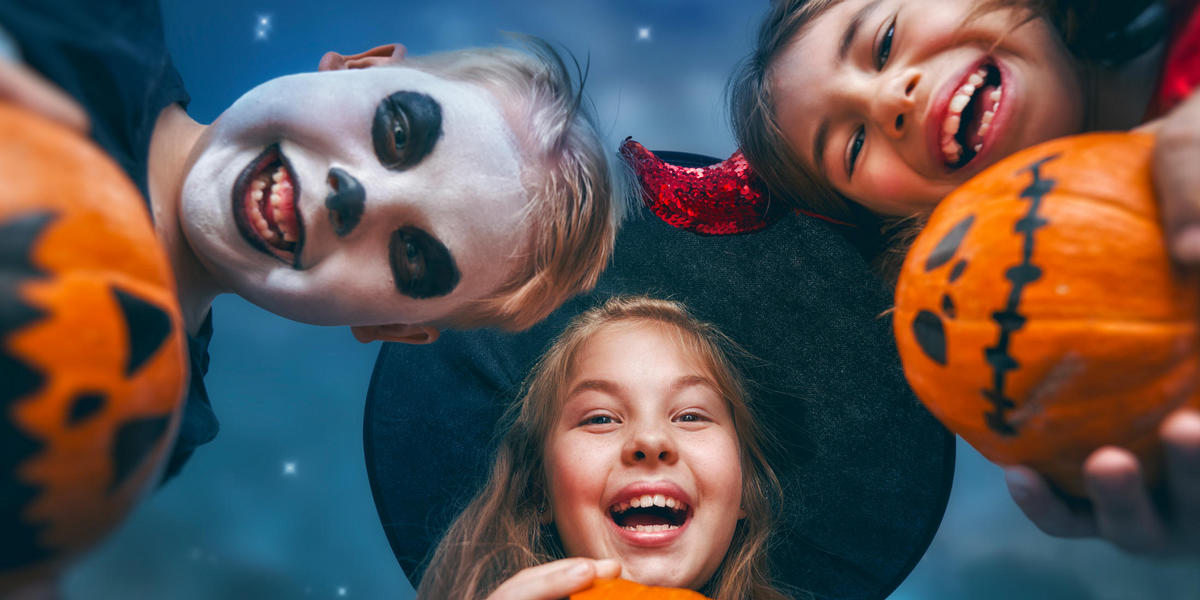 Three kids dressed in Halloween costumes holding pumpkins