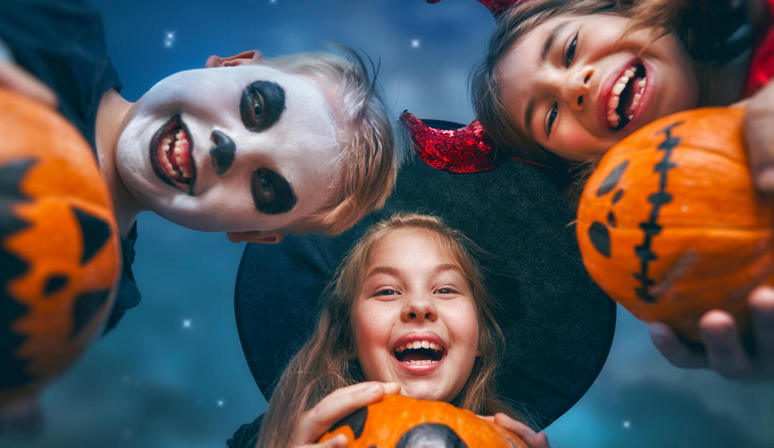 Three kids holding pumpkins dressed in Halloween costumes