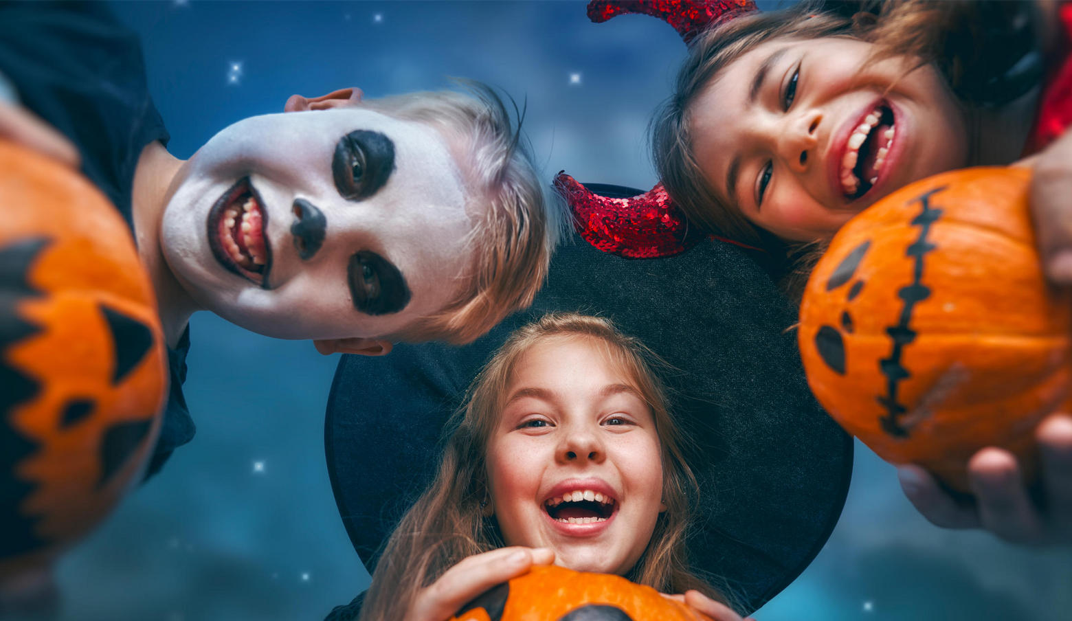 three kids dressed in Halloween costumes holding pumpkins